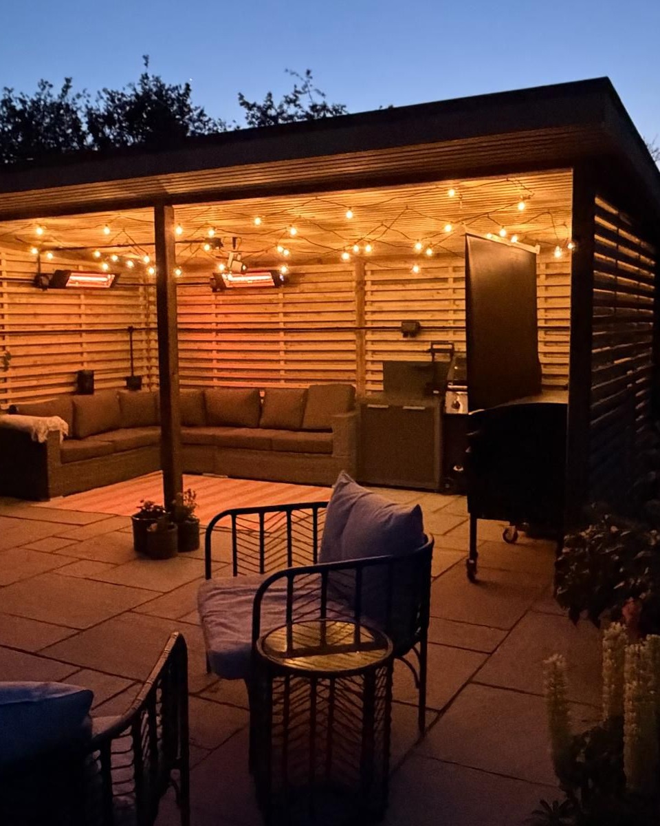 Timber pergola and outdoor shelter with seating and paving, lit at dusk
