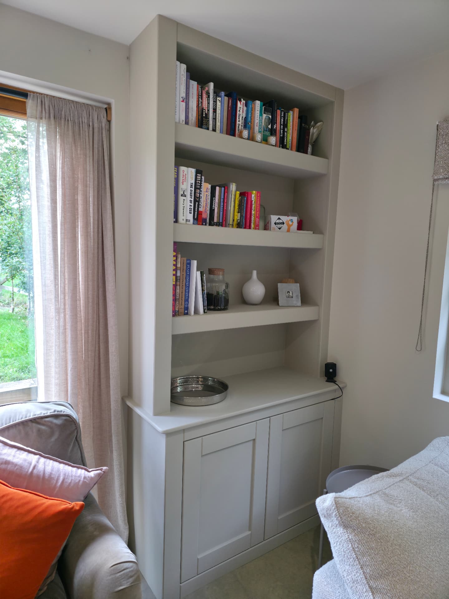 Painted off-white alcove unit with a two-door base cupboard and three floating shelves above, styled with books
