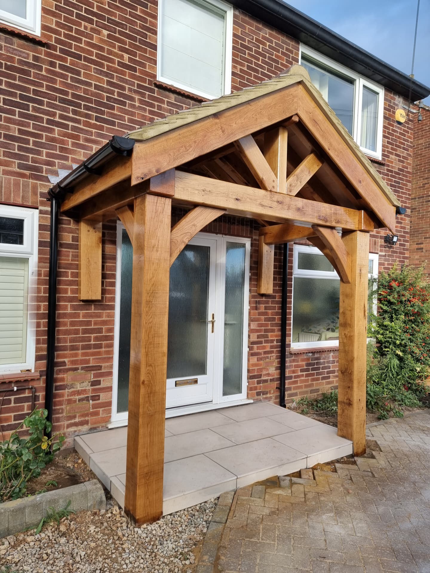 Oak-framed porch with a king-post gable truss and terracotta roof tiles, built against a red brick house with a tiled entrance platform