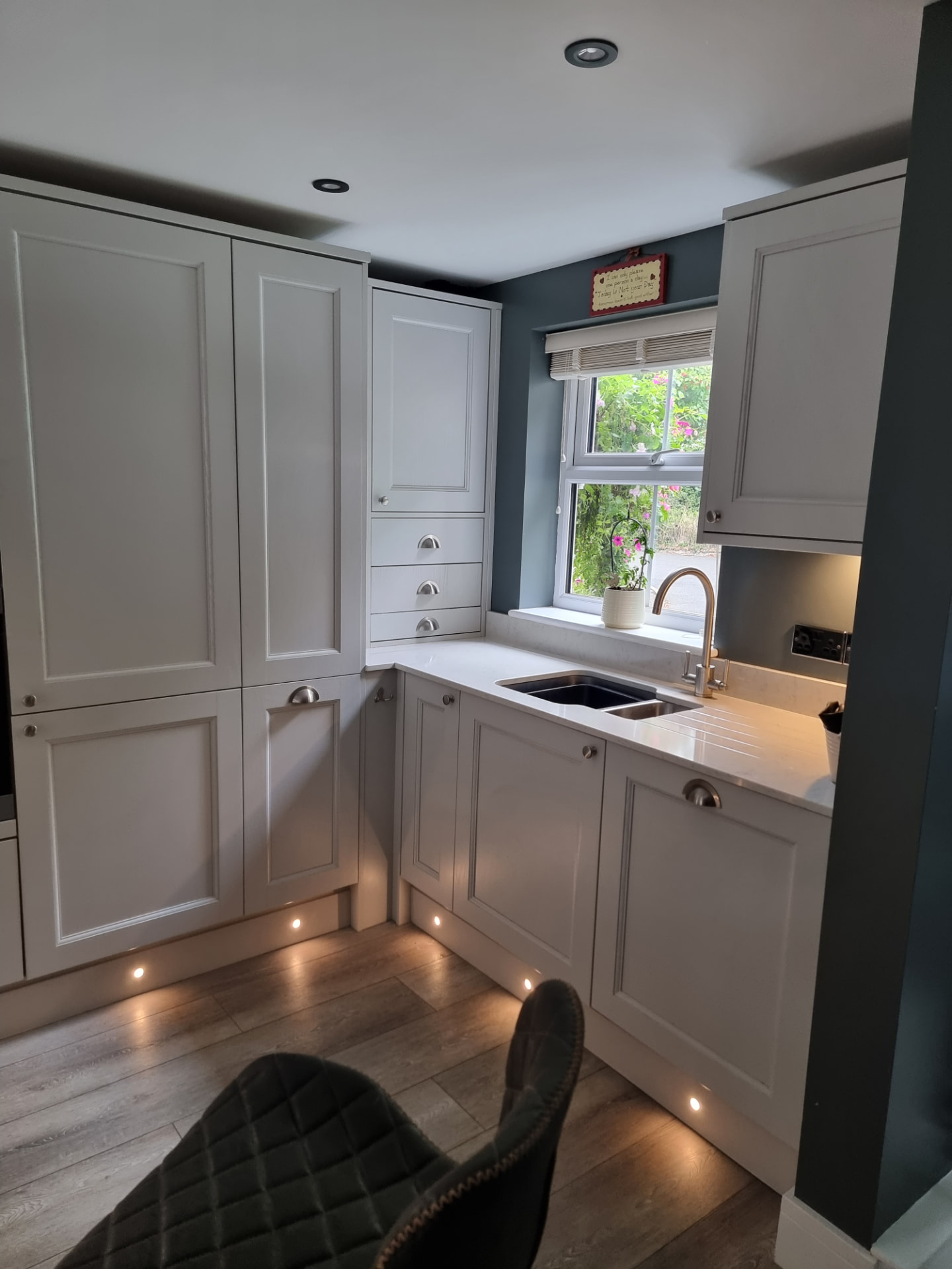 Sink run in the same kitchen, with an undermount sink and swan-neck tap under the window, a quartz worktop with routed draining grooves and floor-to-ceiling shaker units