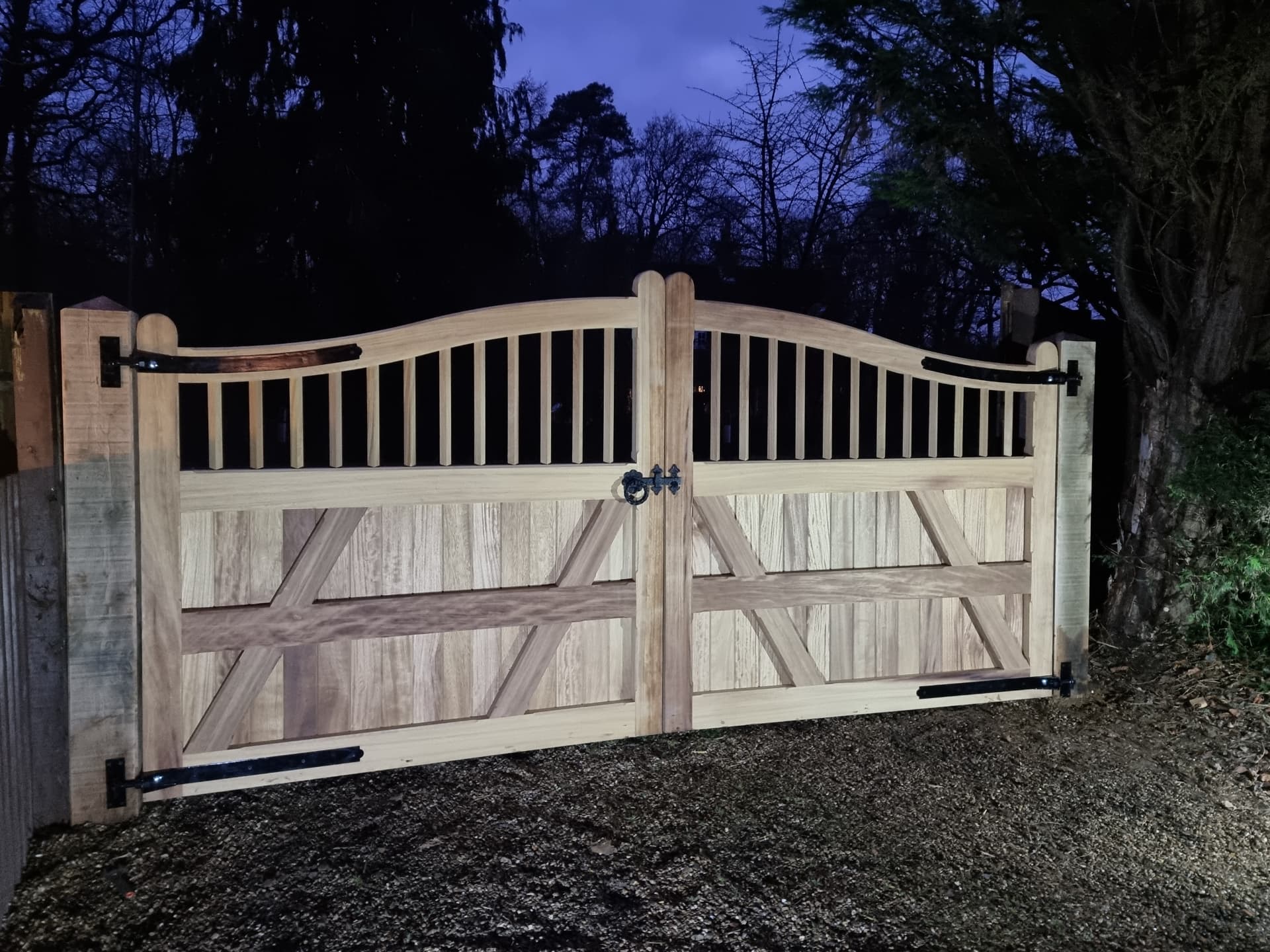 Inside face of the same arched oak gates, showing the diagonal bracing, ledges and heavy iron strap hinges against dark trees