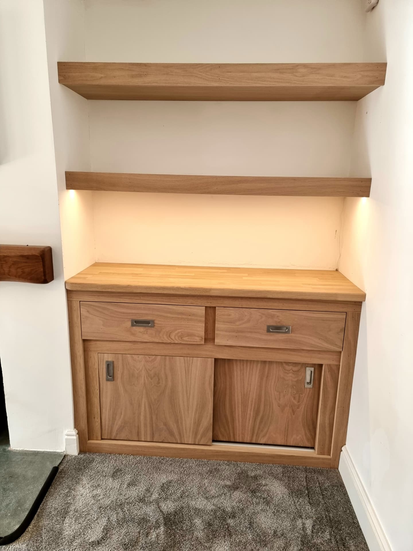 Oak alcove unit beside a fireplace with sliding doors, drawers and lit floating shelves above