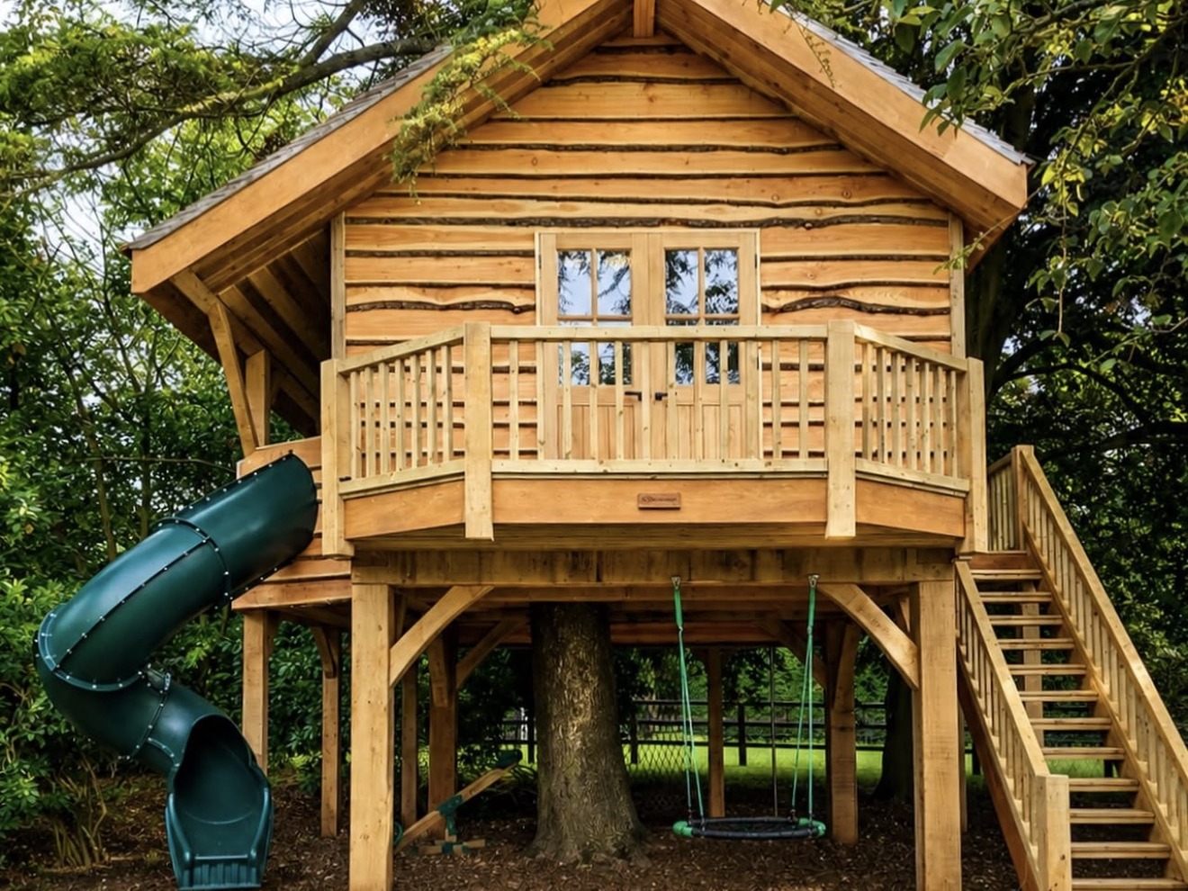 Timber treehouse built among trees, with a balcony, staircase and slide