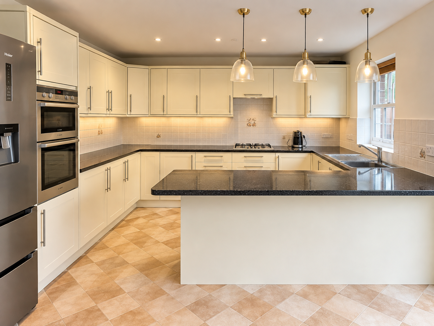 Cream kitchen with a dark stone island, pendant lights and built-in ovens