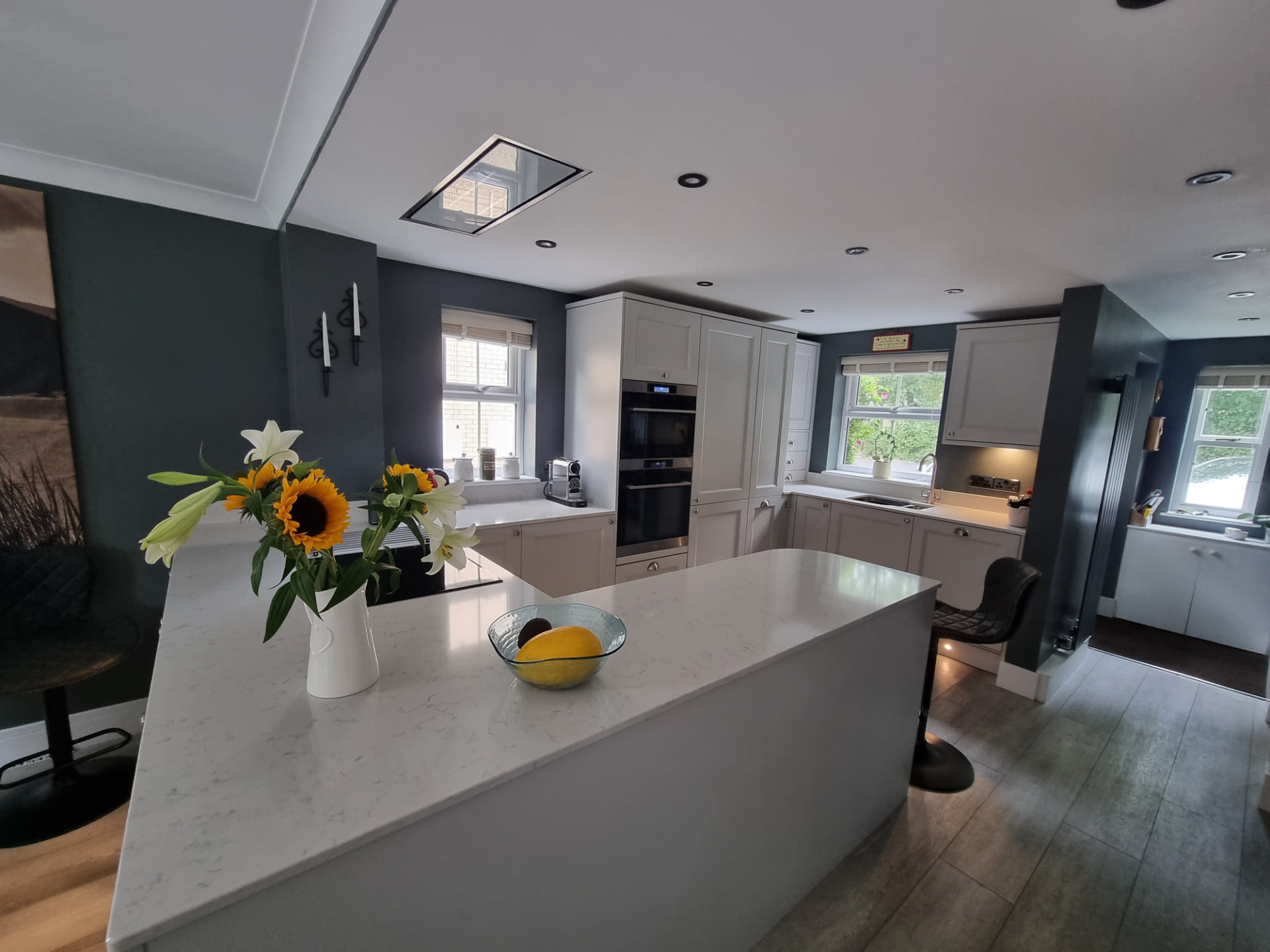 Breakfast bar on the end of the quartz peninsula with stools, looking across to the tall cabinet bank with integrated double ovens