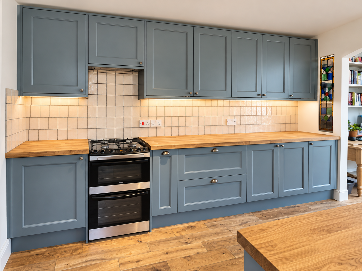 Sage blue shaker kitchen with solid wood worktops, a gas range cooker and a tiled splashback