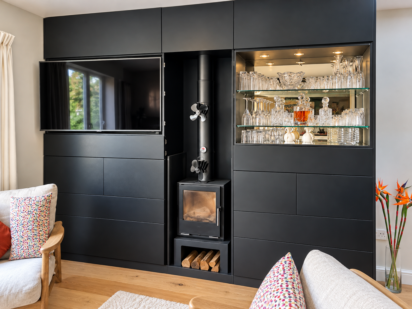 Matte black media wall with a TV, a built-in log burner and wood store, and an illuminated home bar niche with a mirrored back and glass shelves