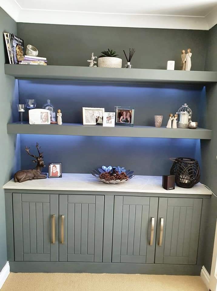 Slate-grey alcove unit with four grooved cupboard doors, a pale stone worktop and two floating shelves with under-shelf lighting