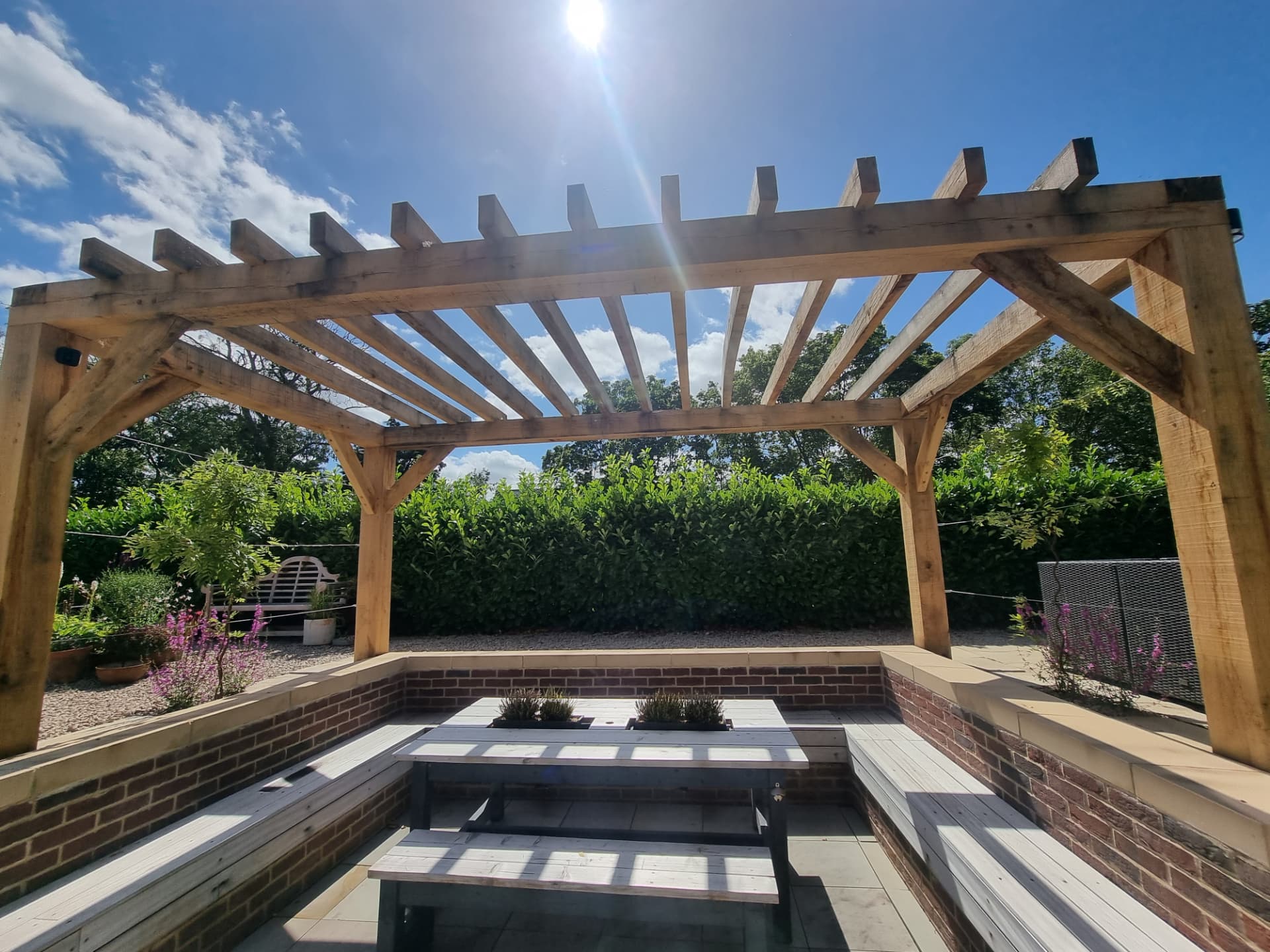 Timber pergola with crossed rafters standing over a sunken stone patio, with brick retaining walls, stone coping and built-in benches